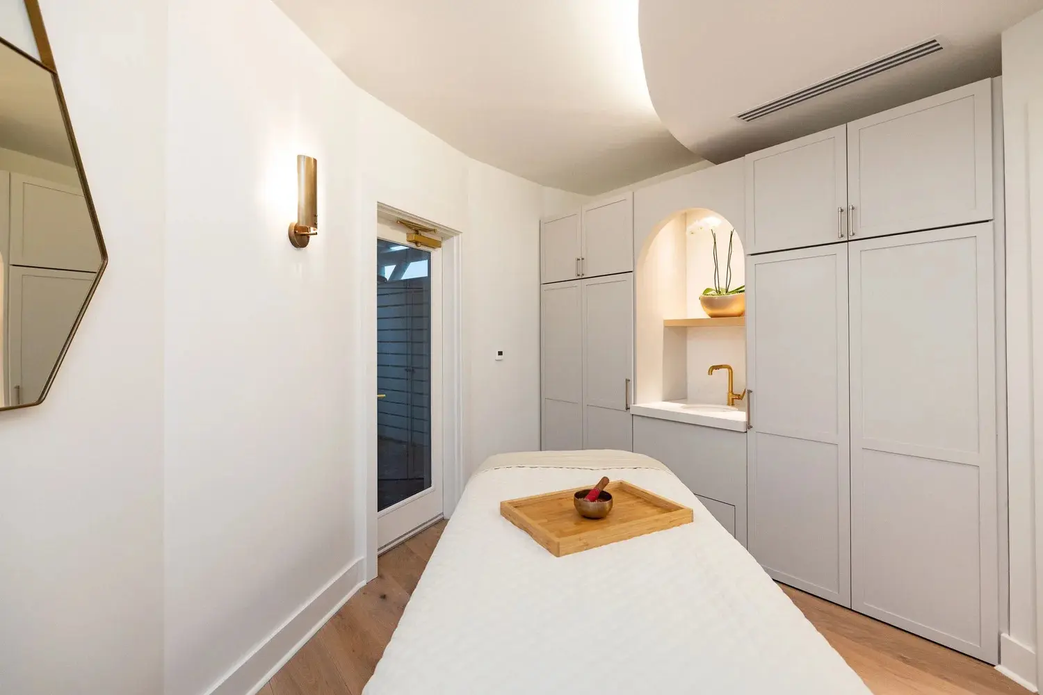 A bright treatment suite with a massage table, sconce lighting and cabinetry